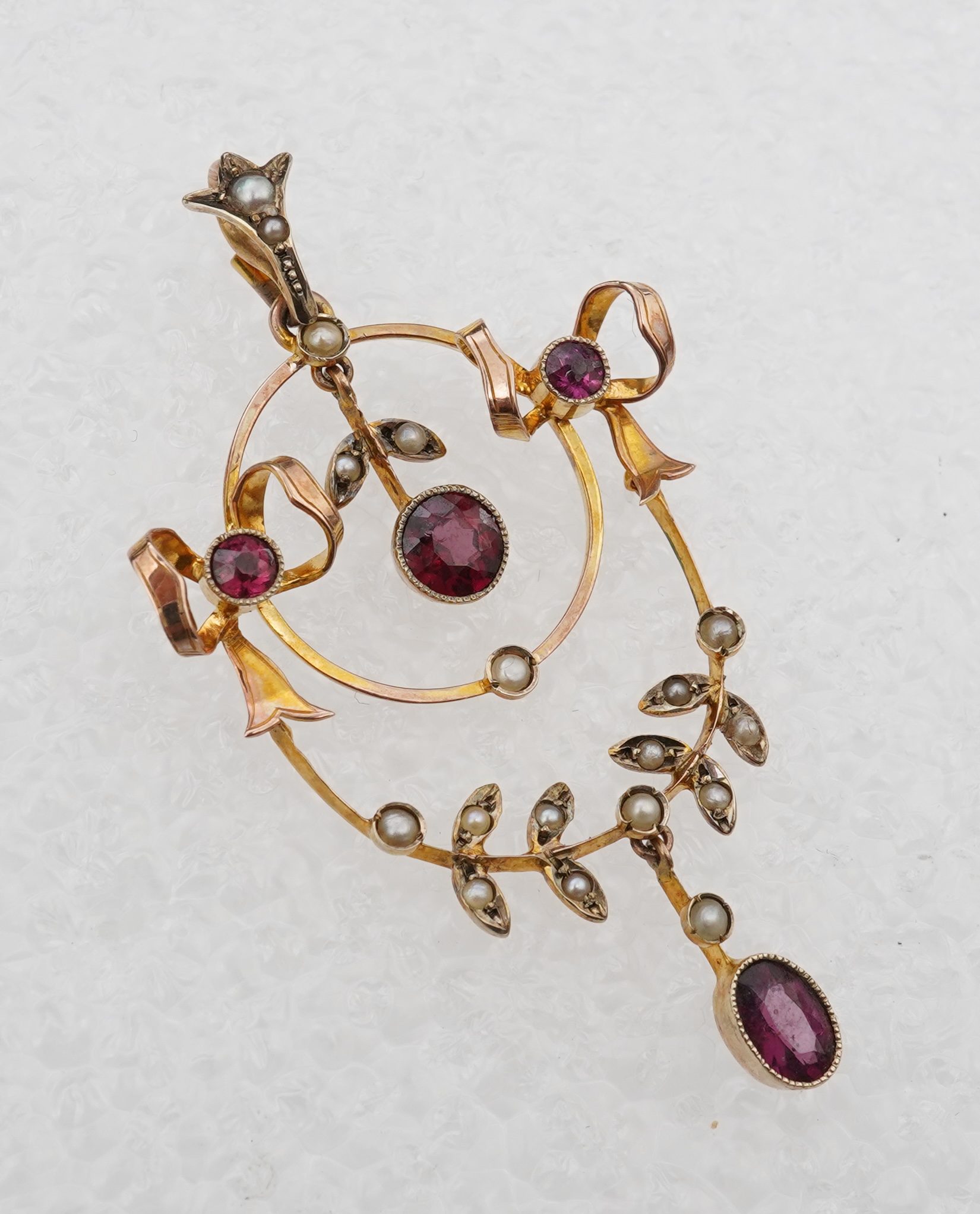 An Edwardian garnet and seed pearl pendant, early 20th century, of foliate design with ribbon bow motifs, set with circular-cut and oval garnets and seed pearls, mounted in gold, length 5.2cm, stamped 9CT, gross weight a
